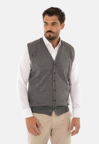 Gilet grigio in maglia con scollatura a V, sei bottoni e orlo a coste, indossato sopra una camicia bianca, esposto su uno sfondo bianco uniforme.