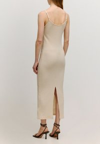 Beiges Midi-Kleid mit strukturiertem Muster, dünnen Trägern und einem Schlitz im Rücken für mehr Bewegungsfreiheit. Kombiniert mit schwarzen Riemchenschuhen.