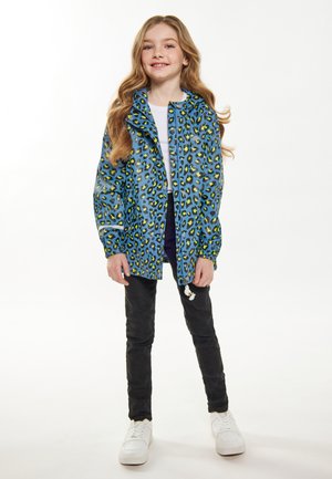 Blå leopardprint jakke med elastiske manchetter, parret med sorte bukser og hvide sneakers. Glat tekstur og afslappet, lagdelt design.