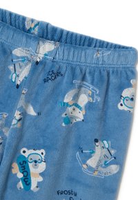 Pyjamas en polaire bleue avec des motifs de ours polaire et de renard amusants, accompagnés d'accessoires comme des lunettes de protection et des planches de snowboard. Ceinture élastique incluse.