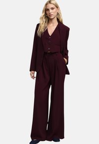 Completo tre pezzi bordeaux con gilet aderente con bottoni, pantaloni a gamba larga e blazer monopetto con un bottone. Tessuto liscio con design sartoriale.