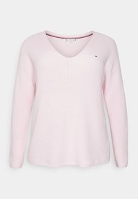 Pull en maille rose clair avec un col en V, manches longues, texture côtelée et un détail subtil sur le côté. Comprend un petit logo sur la poitrine.