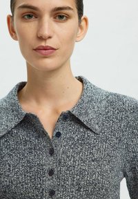 Marinblå och grå mönstrad stickad polo med krage, sex svarta knappar och en texturerad yta.