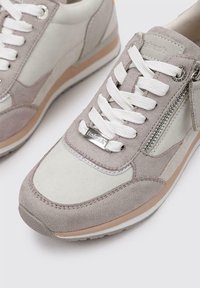 Zapatillas de deporte en gris claro y beige, con materiales de gamuza y cuero, que cuentan con cordones blancos, un zipper lateral y un sutil acento marrón claro en la suela.
