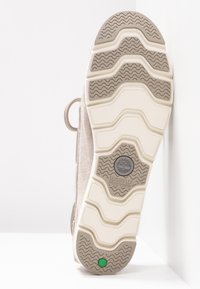 Semelle de chaussure beige clair en caoutchouc texturé, avec un motif en vagues et un accent hexagonal vert. Conception légère intégrant des éléments de rembourrage.