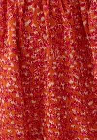Tissu rouge-orange avec un motif floral agrémenté de touches de blanc et de rose. Surface texturée avec des plis pour plus de détails.
