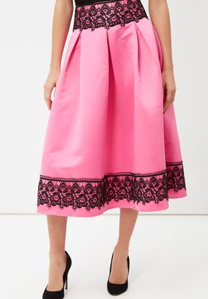 Mujer con falda midi rosa con encaje negro en la cintura y el dobladillo, combinada con zapatos de tacón negros.