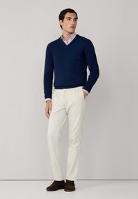 Suéter de punto en color navy con cuello en V sobre una camisa a rayas rosa y blanca, combinado con pantalones blancos y zapatos de ante marrón. Texturas suaves, ajuste a medida.