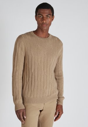 Beige gebreide trui met een gestructureerd rib ontwerp, ronde halslijn en lange mouwen, gecombineerd met lichtgekleurde broeken.