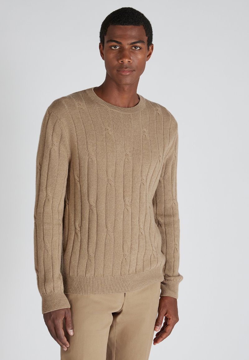 Beige gestrickter Pullover mit strukturiertem Rippdesign, Rundhalsausschnitt und langen Ärmeln, kombiniert mit hellen Hosen.