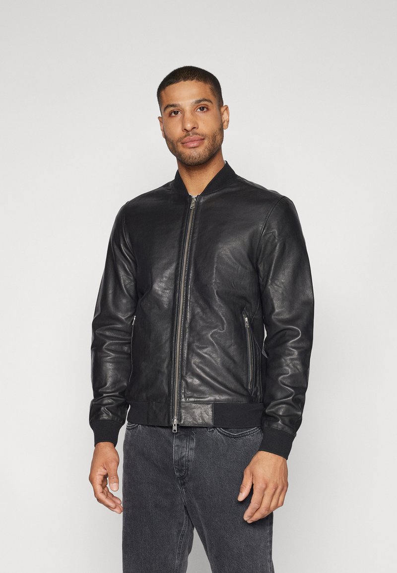 Veste bomber en cuir noir avec fermeture éclair, poignets et ourlet côtelés, et poches latérales. Texture lisse, design ajusté.