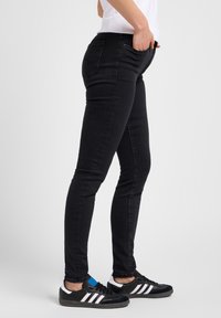 Jean skinny noir en denim, avec un design classique à cinq poches et un léger stretch pour le confort. Portés avec des baskets noires.