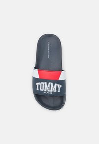 Infradito blu navy con suola testurizzata. Presenta una fascia larga in rosso, bianco e blu navy con il logo "TOMMY HILFIGER" stampato in nero.