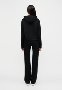 Μαύρο βαμβακερό φούτερ με κουκούλα και κορδόνια, συνδυασμένο με άνετο, μαύρο φόρμα παντελόνι, και τα δύο με απαλή υφή και μίνιμαλ σχεδιασμό.