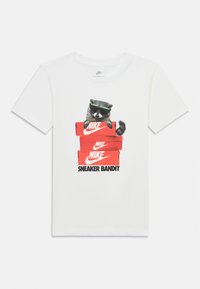 T-shirt branco de algodão com uma guaxinim de óculos de sol, empilhado em caixas de sapatos vermelhas da Nike com a inscrição "SNEAKER BANDIT" abaixo.