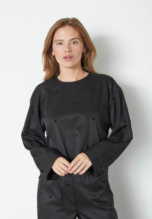 Top lungo in satin nero a maniche lunghe con scollo rotondo, caratterizzato da pois ricamati e una vestibilità rilassata. Dettagli con bottoni sulle maniche.