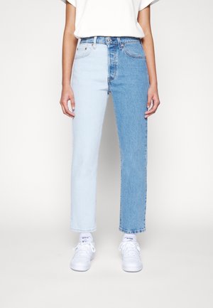 Person iført højtaljede jeans med det ene ben lys blå og det andet ben mellemblå, kombineret med hvide sneakers og en hvid top.