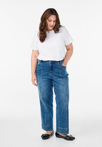 Modré džínsy s vysokým pásom a voľným strihom, dve predné vrecká a viditeľným prešívaním. Skombinované s bielym tričkom a čiernymi balerínkami.