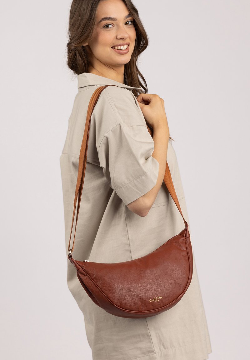 Braune Leder-Schultertasche mit runder Form, verstellbarem Tragegurt und einem dezenten Logo. Glatte Textur und minimalistisches Design.