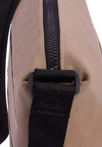 Bolso de nylon beige con cremallera negra. Cuenta con una gruesa correa negra unida con un clip de plástico negro duradero. Textura suave, diseño minimalista.