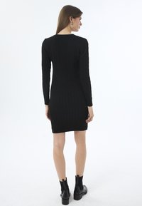 Must musträtik, millel on pikad varrukad, millel on kaablikud templid ja ribakujundus. Kombineeritud mustade pahkluu kingadega.