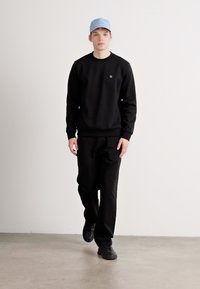 Sort sweatshirt med rund halsudskæring og lille logo, parret med sorte bukser og sorte sneakers. Lyseblå cap tilføjer farve.