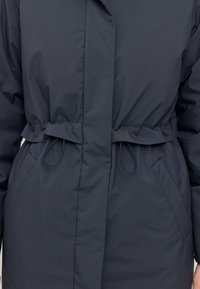 Doudoune bleu marine foncé avec ceinture à nouer, poches latérales et détail logo discret. Texture lisse, tissu léger et chaud.