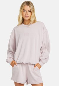 Light pink sweatshirt with textured logo and relaxed fit; paired with matching shorts featuring pockets and logo detailing.