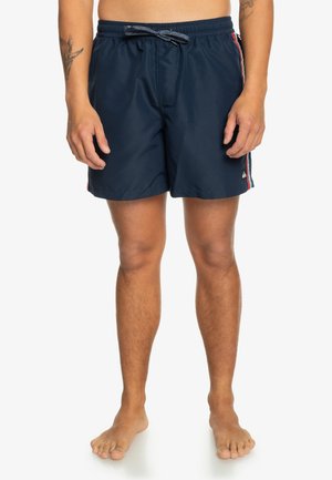Bañador de color navy con cintura elástica, cordón ajustable, rayas laterales en rojo y verde azulado, y un logo en la parte inferior izquierda.