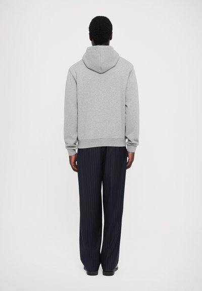 Sweatshirt à capuche gris avec une coupe décontractée, associé à un pantalon bleu marine à rayures. Le tissu a l'air doux et texturé.
