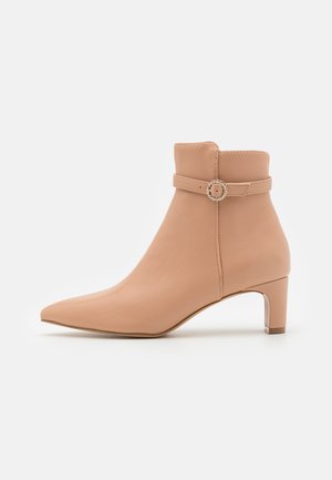 Bottines en cuir beige avec un bout pointu, une tige courte et une sangle décorative avec une boucle ronde. Talon bloc avec accent transparent.