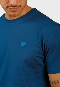 Camiseta de algodón azul marino con cuello redondo, que presenta un pequeño logotipo de elefante azul en el pecho. Textura suave y con mangas cortas.