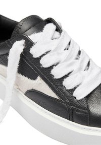 Black leather sneaker with white fuzzy laces and a textured canvas side panel. Features a raised white rubber sole and stitching detail.