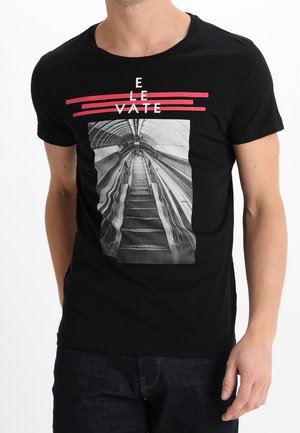 T-shirt en coton noir présentant un graphisme d'escaliers mécaniques, avec le texte 'ELEVATE' en rose au-dessus de l'image. Manches courtes et col rond.