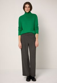 Grüner, gestrickter Rollkragenpullover mit Strickmuster, kombiniert mit weit geschnittenen, anthrazitgrauen Nadelstreifenhosen und schwarzen Stiefeletten.