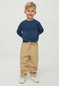 Niebieska koszula z długim rękawem, w połączeniu z beżowymi spodniami z elastycznym paskiem i białymi trampkami. Gładki materiał, luźny krój i prosty design.