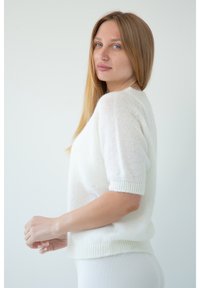 Biała sweter z krótkim rękawem, o luźnym kroju i ribbowanym wykończeniu. Tekstura wydaje się miękka i lekka.