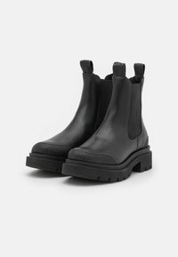 Botas de cuero negro hasta el tobillo con paneles laterales elásticos, punteras texturizadas y suelas de goma gruesas. Presentan tiradores para una fácil colocación.