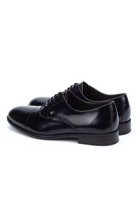 Pair of polished black leather Oxford dress shoes with closed lacing and low stacked heels on a white background.