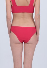 Ensemble bikini rouge avec un design sans couture, des larges bretelles et un bas offrant une couverture moyenne avec une texture lisse. Pas de matériel visible ni de motifs.