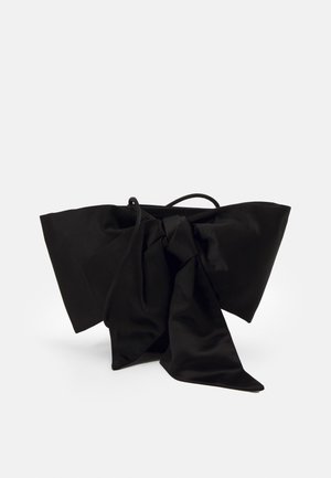 Czarna materiałowa torba z dużą kokardą i cienkim paskiem, prezentowana na białym tle.