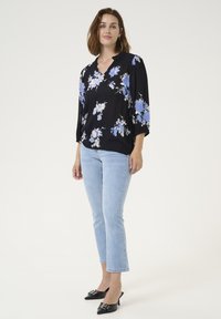 Blusa floreale con motivi blu e bianchi su sfondo nero, caratterizzata da scollo a V e maniche a tre quarti, abbinata a jeans azzurri chiari e tacchi neri.