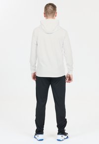 Lys grå langærmet hoodie med hætte, parret med sorte træningsbukser. Stoffet ser glat ud; bukserne har elastiske manchetter og en tætsiddende pasform.