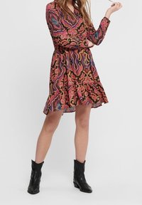 Robes à manches longues, longueur genoux, en tissu à motifs rose, violet et noir avec un ourlet évasé et un décolleté en V, associées à des bottines noires.