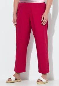 Rote, leichte Baumwollhosen mit elastischem Bund, geradem Beinanschnitt und subtiler Schimmerung. Kombiniert mit weißen Sandalen, die einen Schleifenakzent haben.