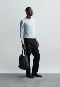 Lys grå langermet genser med et lite logo, svarte bukser og en svart skulderveske. Glatt tekstur, tilpasset passform og minimalistisk design.