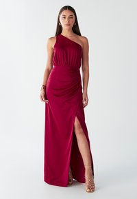 Viens plecs, bordo sarkana satīna kleita ar rievotu jostasvietu un augstu šķēlumu. Raksturo gluda tekstūra un plūstoša siluets. Valkāta ar zelta siksniņu papēžiem.