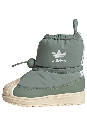 Wysokie zimowe buty Adidas w stonowanym zielonym kolorze z elastycznym zamknięciem na sznurek, białą podeszwą, teksturowaną osłoną palców i logo Adidas na kostce.