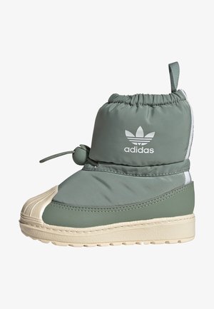 Wysokie zimowe buty Adidas w stonowanym zielonym kolorze z elastycznym zamknięciem na sznurek, białą podeszwą, teksturowaną osłoną palców i logo Adidas na kostce.