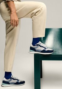 Sportowe sneakersy w połączeniu granatowego, jasnoszarego i białego materiału. Posiadają teksturowaną cholewkę, wyściełany kołnierz oraz białą podeszwę.